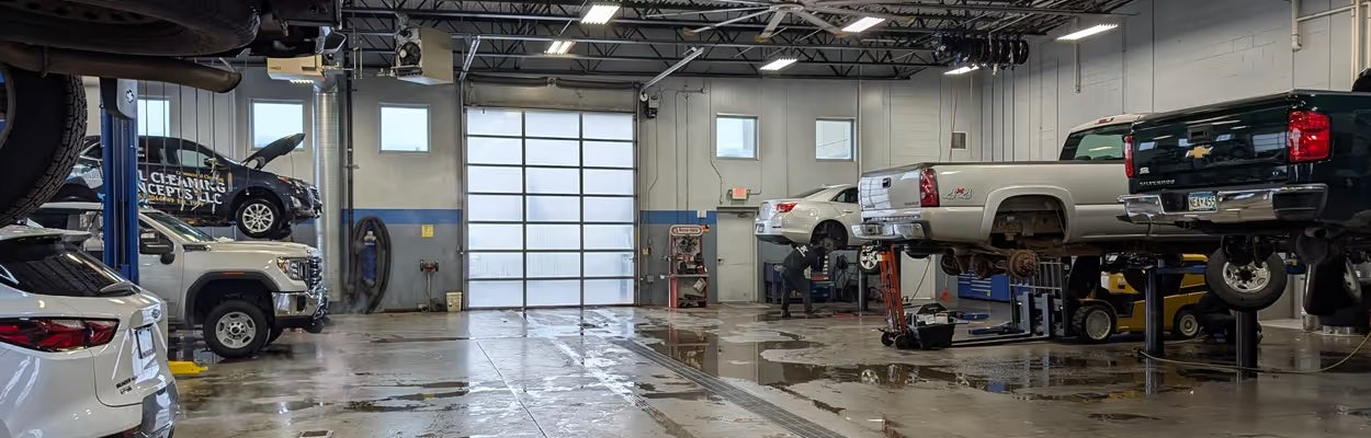 Busy auto repair shop with multiple vehicles on hydraulic lifts, some being worked on, and wet, shiny floors.